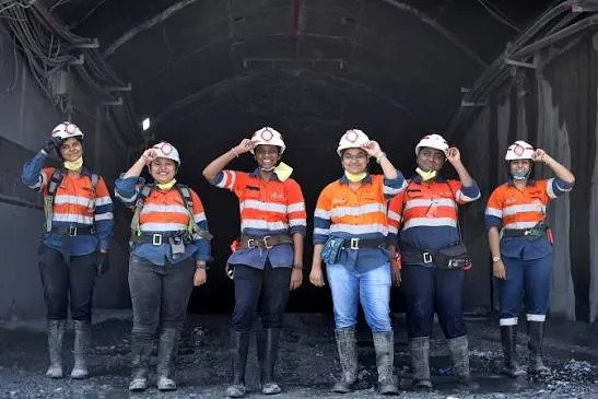Six women mining professionals in hard hats and high-visibility uniforms at an underground mine entrance